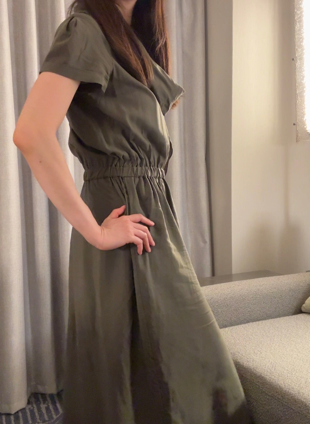 Person wearing a green dress standing indoors with curtains in the background