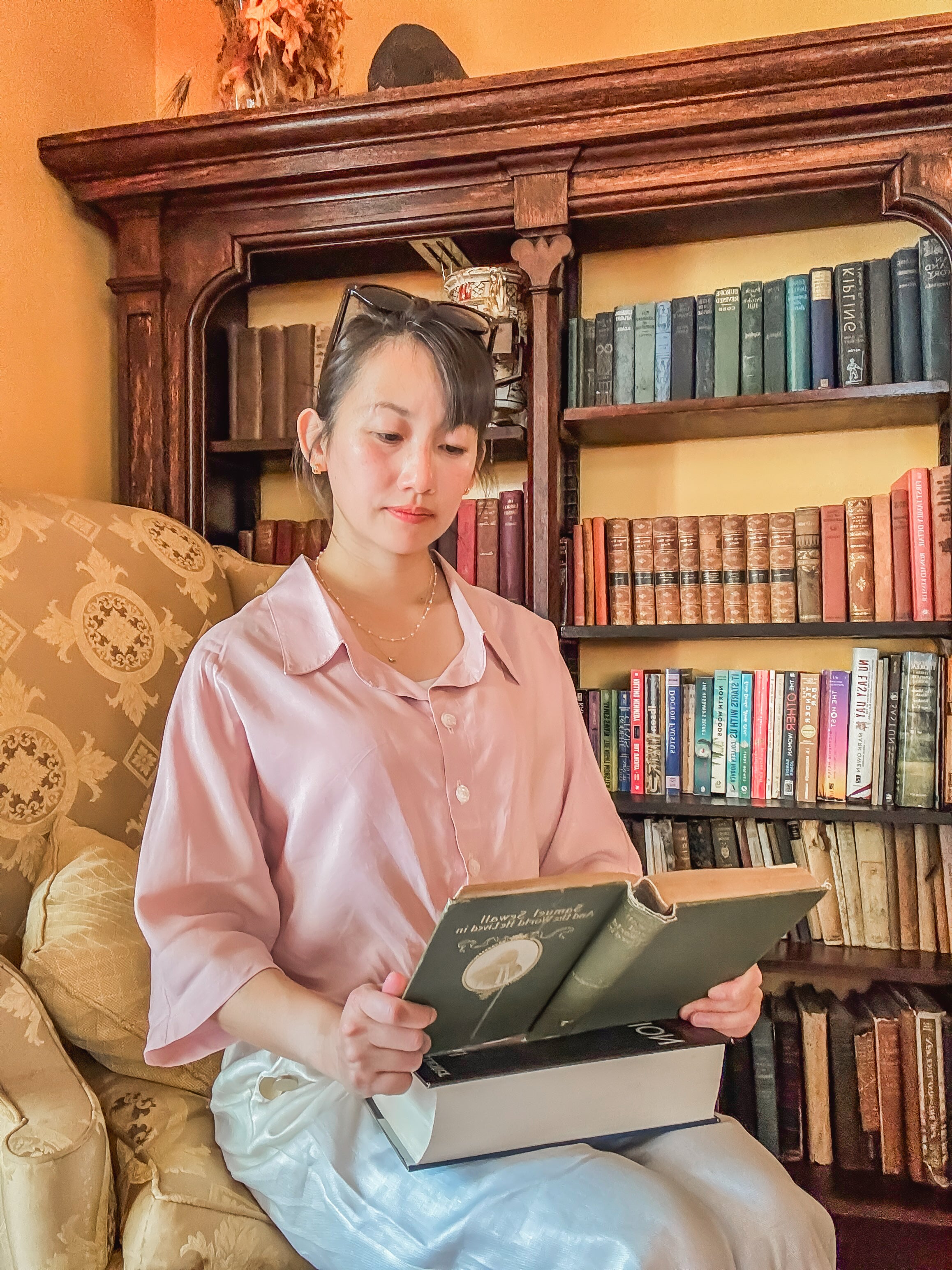 Woman holding a book in a room filled with books and decorative elements.