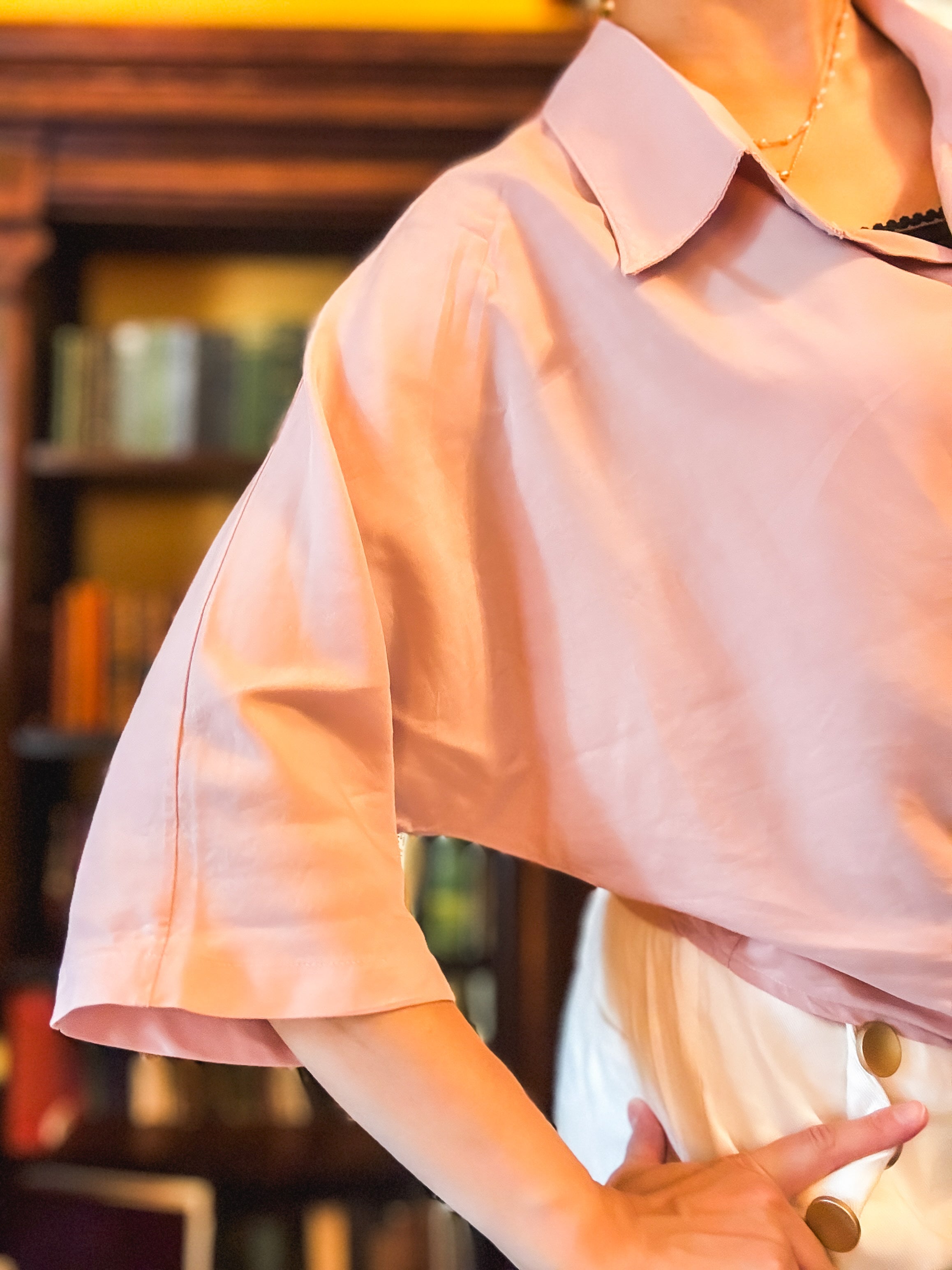 Person wearing a light pink shirt with a blurred bookshelf background